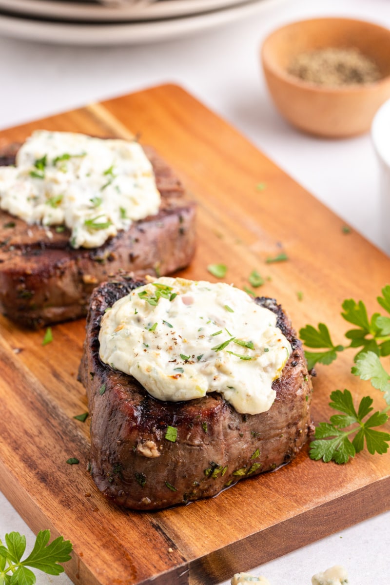 two steaks on a cutting board topped with blue cheese sauce