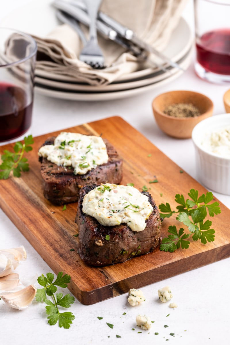 two steaks on a cutting board topped with blue cheese sauce