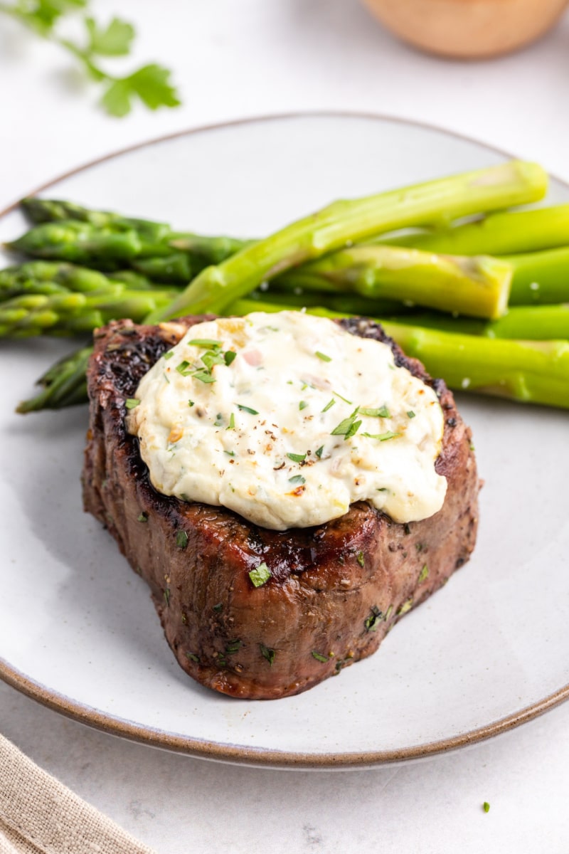 grilled steak with blue cheese and chiles served on white plate with asparagus