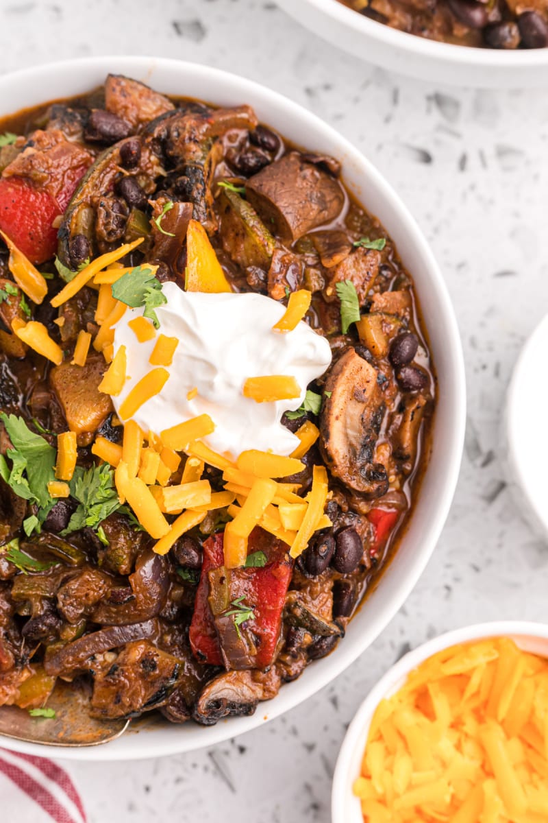 grilled vegetable chili in white bowl garnished by sour cream and cheese