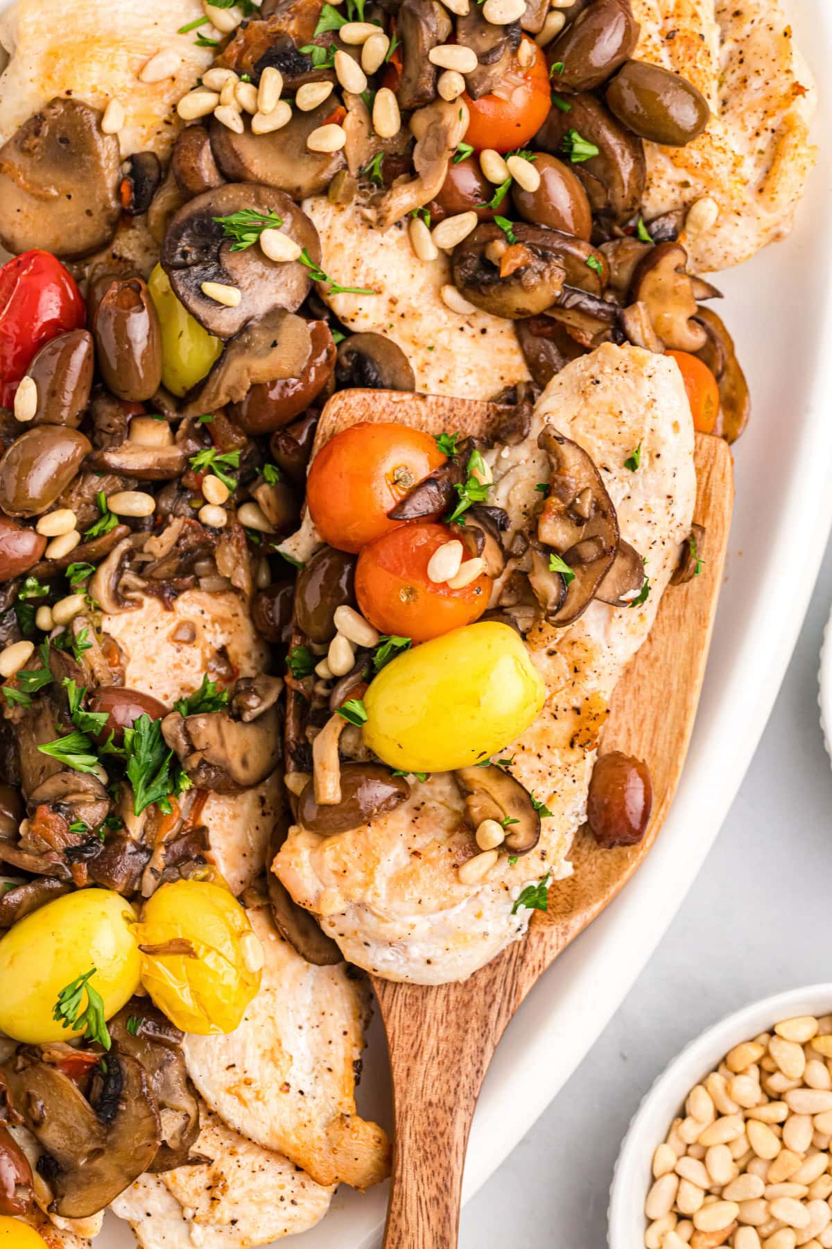 A recipe for sautéed Mediterranean Chicken with big flavors of tomato, garlic, mushrooms, olives, capers and pine nuts. Recipe from RecipeGirl.com. spatula picking up serving of mediterranean chicken