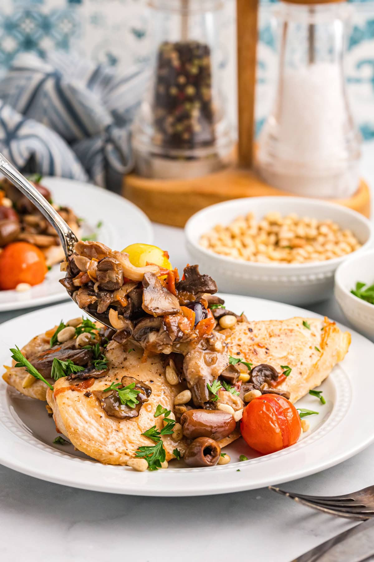 A recipe for sautéed Mediterranean Chicken with big flavors of tomato, garlic, mushrooms, olives, capers and pine nuts. Recipe from RecipeGirl.com. spooning topping onto mediterranean chicken