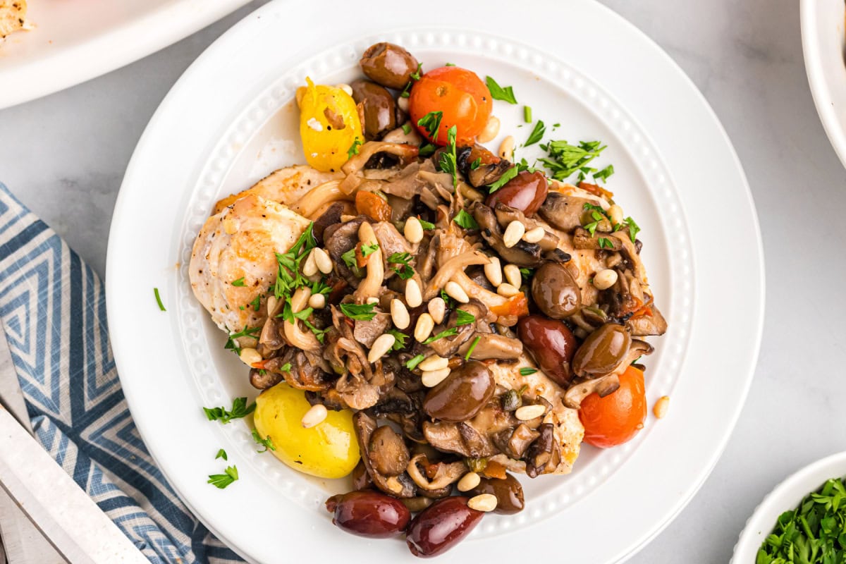 A recipe for sautéed Mediterranean Chicken with big flavors of tomato, garlic, mushrooms, olives, capers and pine nuts. Recipe from RecipeGirl.com. serving of mediterranean chicken on a plate