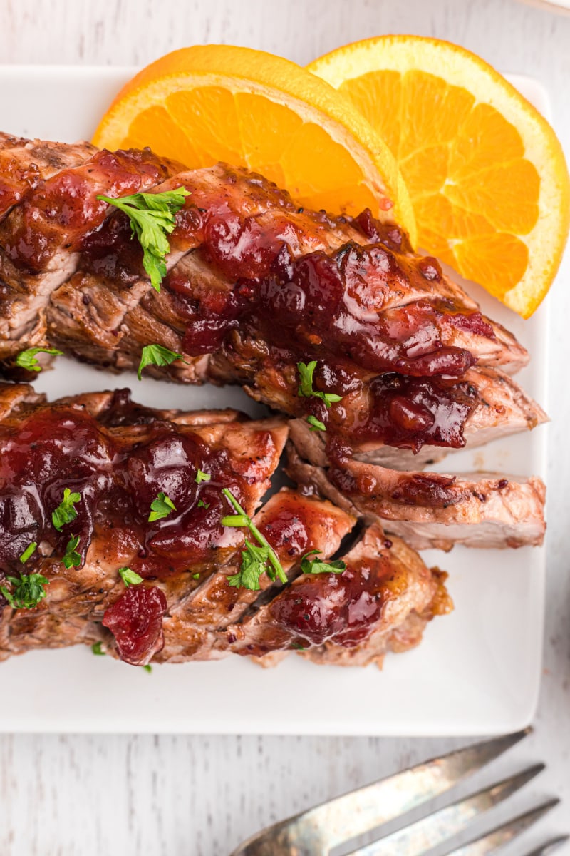 sliced orange cranberry glazed pork tenderloin on a platter with fresh oranges