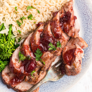 serving of orange cranberry glazed pork tenderloin on a plate with rice and broccoli