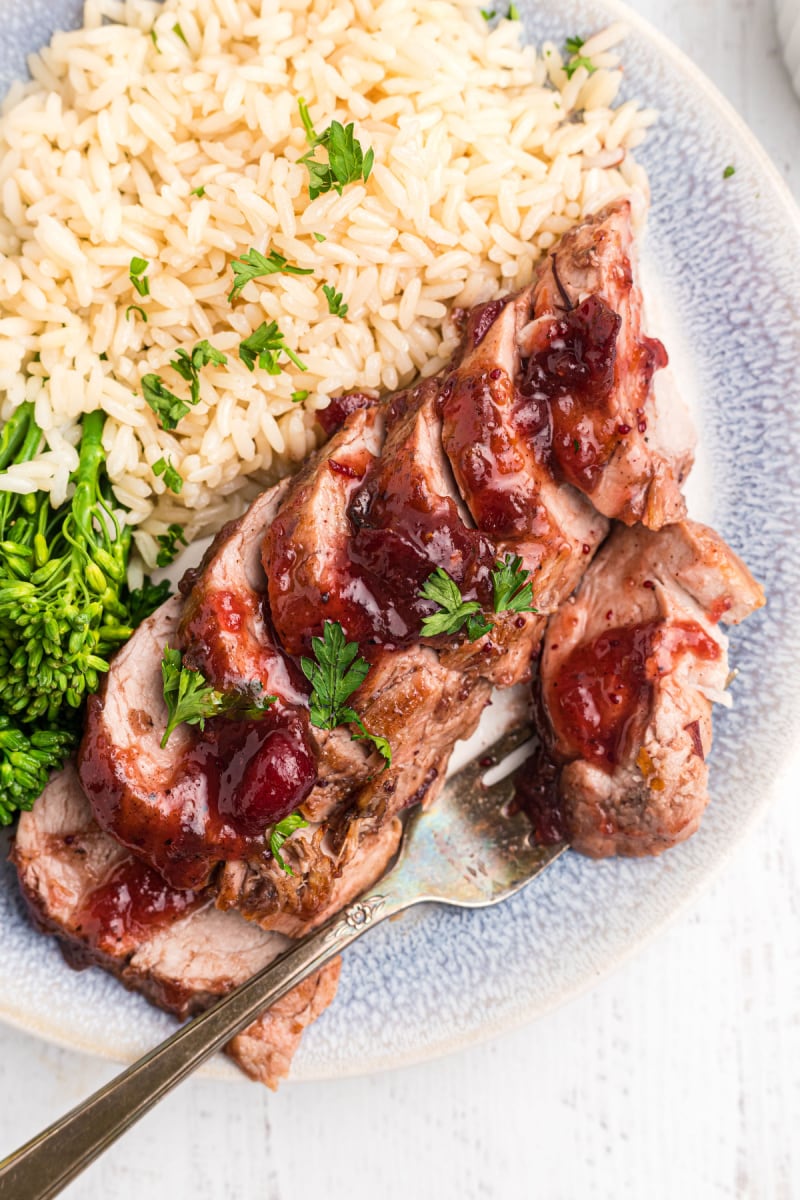 serving of orange cranberry glazed pork tenderloin on a plate with rice and broccoli