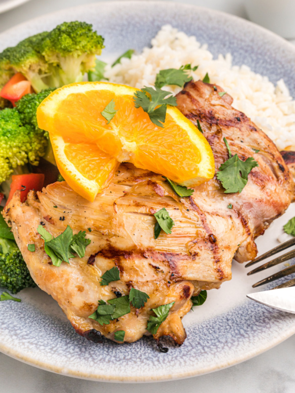 orange and ginger grilled chicken thigh on plate with orange slice on top