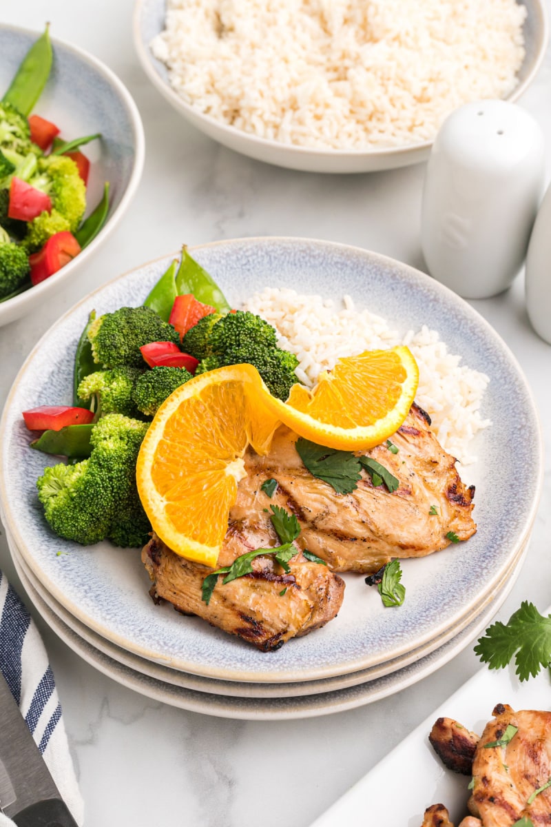orange and ginger grilled chicken thigh on plate with orange and broccoli