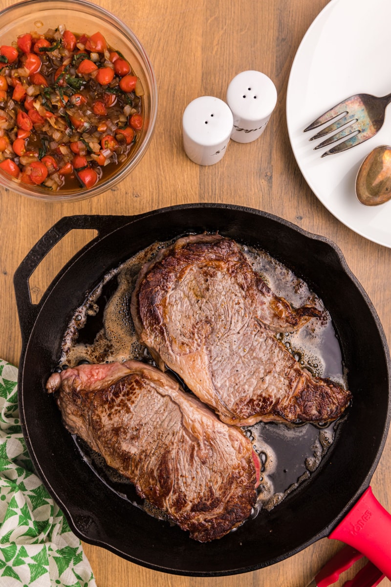 two steaks frying in cast iron skillet