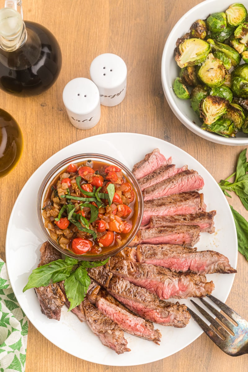 sliced steak on plate with bowl of salsa