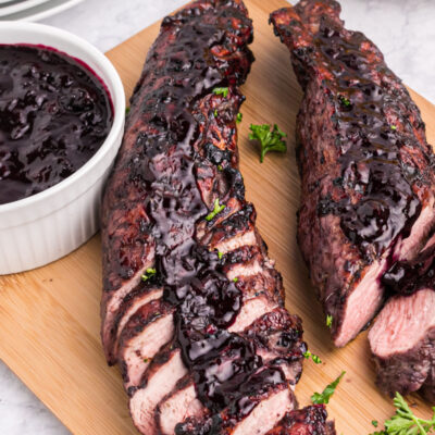 grilled pork tenderloin on a board topped with blueberry BBQ Sauce