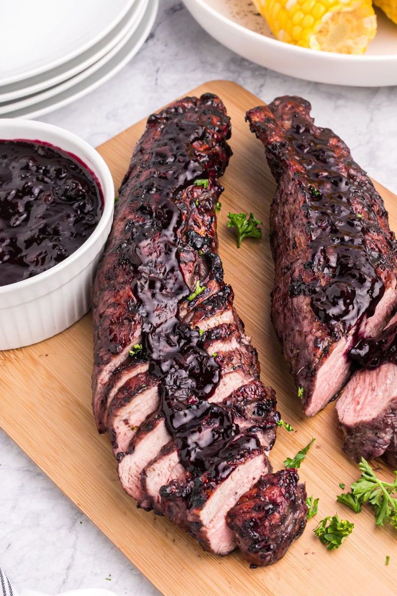 grilled pork tenderloin on a board topped with blueberry BBQ Sauce