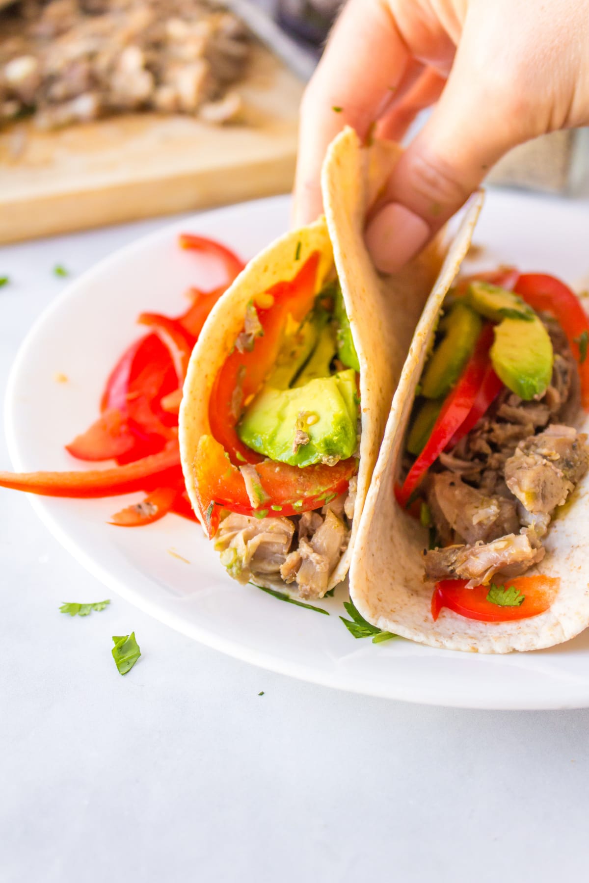 hand picking up carnitas tacos on plate