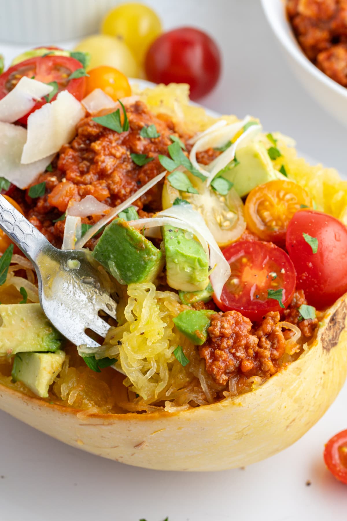 fork in a half spaghetti squash with spicy meat sauce and garnishes