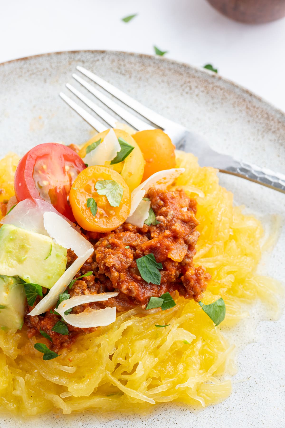 serving of spaghetti squash on plate topped with spicy meat sauce and garnishes
