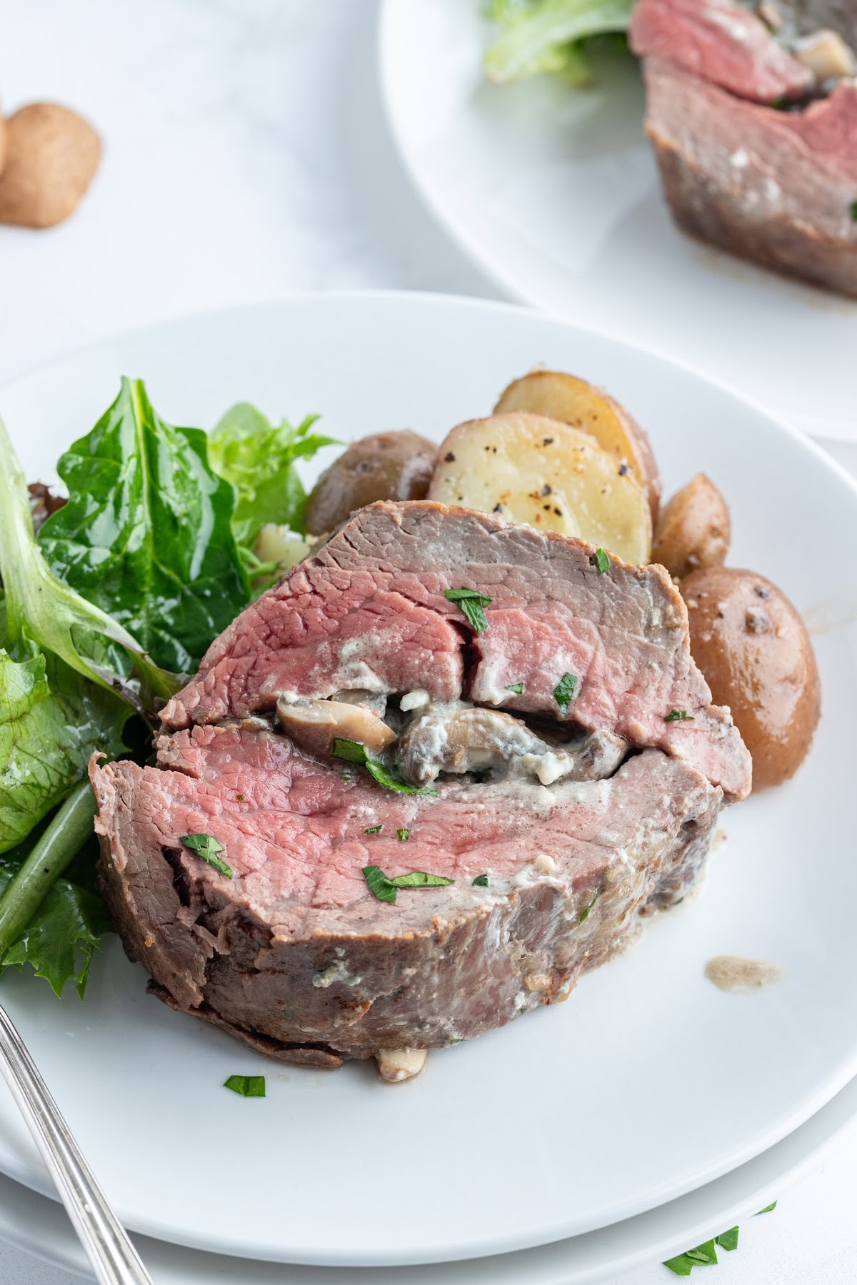 Elegant stuffed beef tenderloin filled with mushrooms, garlic, green onions, and blue cheese. A stunning holiday or special-occasion dinner that’s surprisingly easy! slice of stuffed beef tenderloin on a plate with salad