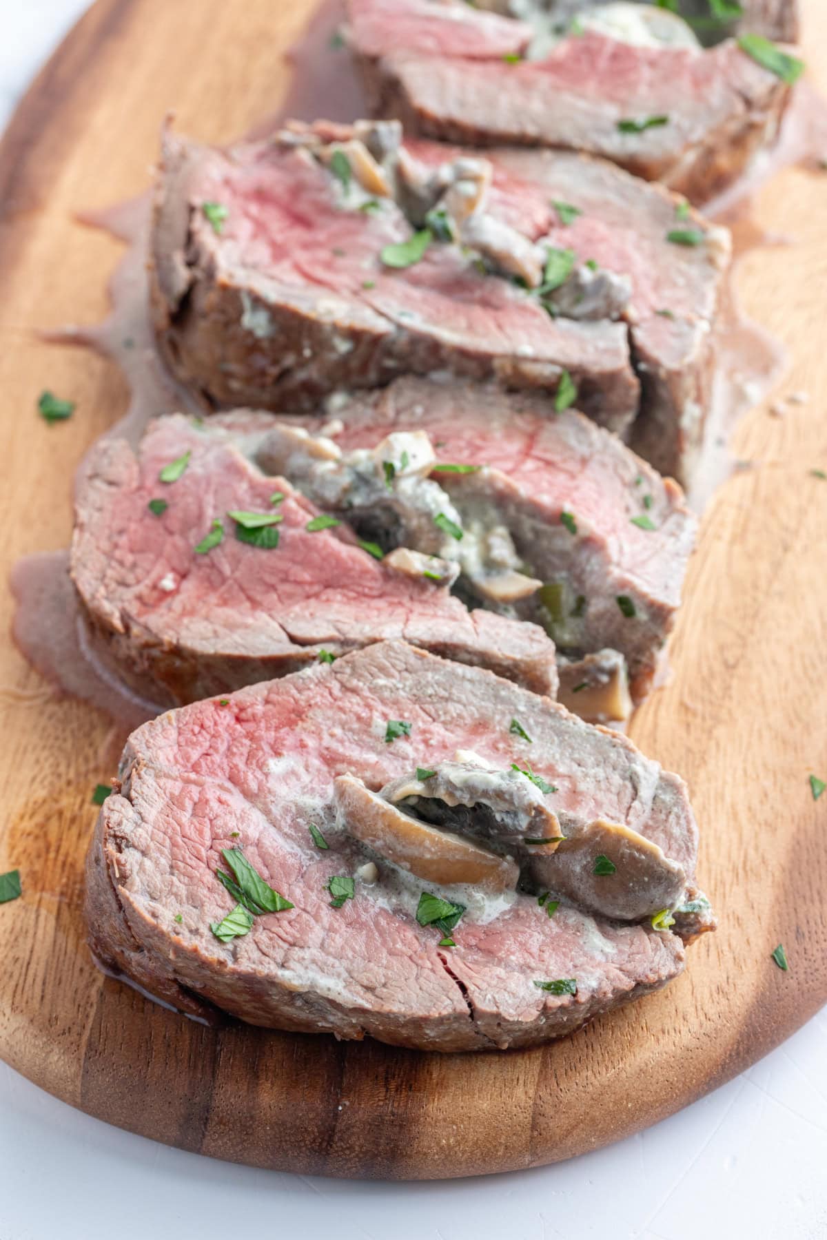 Elegant stuffed beef tenderloin filled with mushrooms, garlic, green onions, and blue cheese. A stunning holiday or special-occasion dinner that’s surprisingly easy! stuffed beef tenderloin cut into slices on board