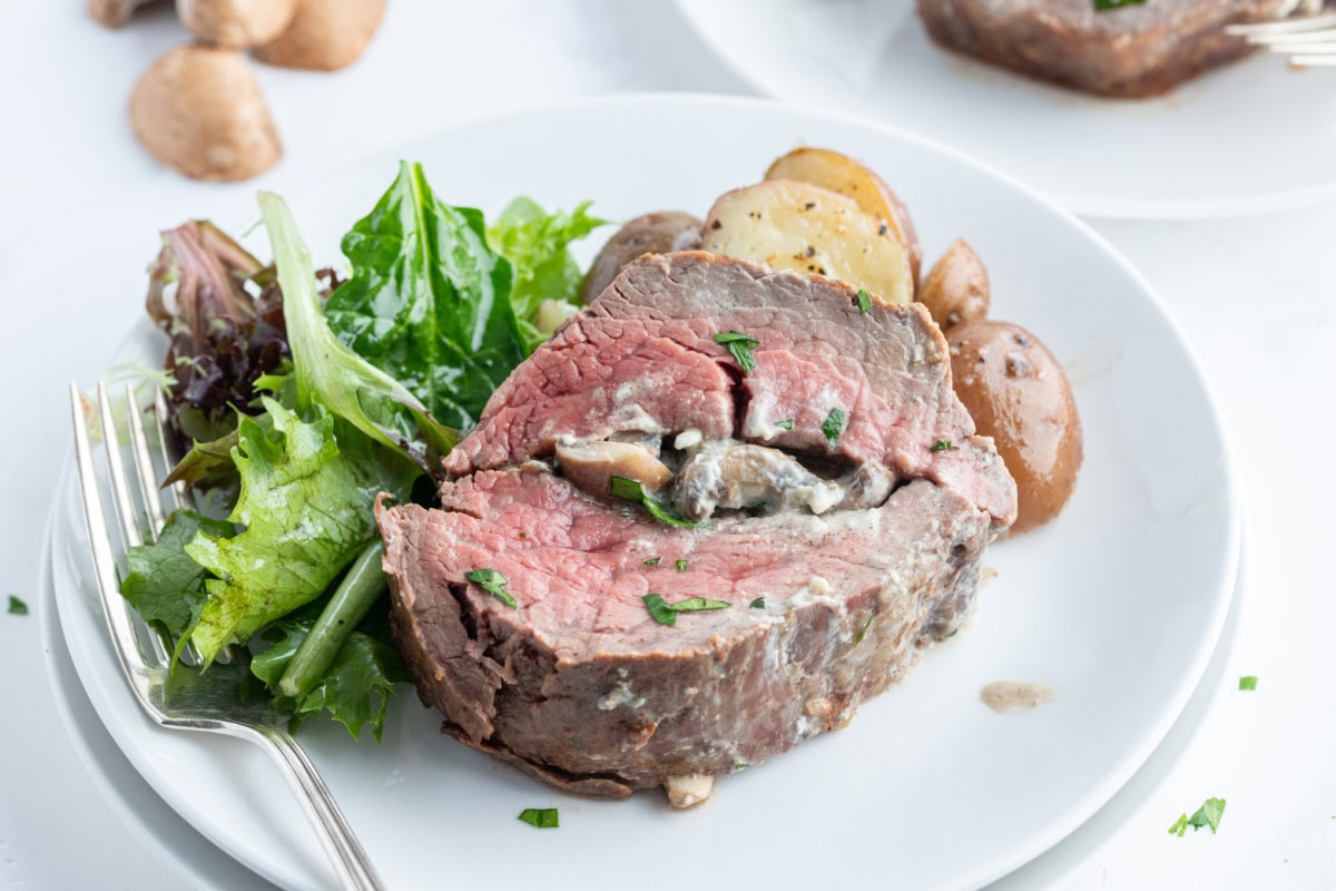 Elegant stuffed beef tenderloin filled with mushrooms, garlic, green onions, and blue cheese. A stunning holiday or special-occasion dinner that’s surprisingly easy! stuffed beef tenderloin with salad on plate