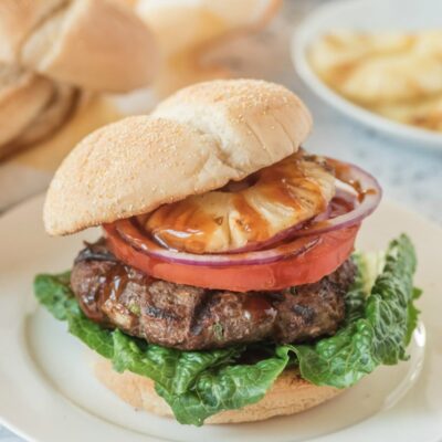 teriyaki burger with bun on top sitting on a white plate