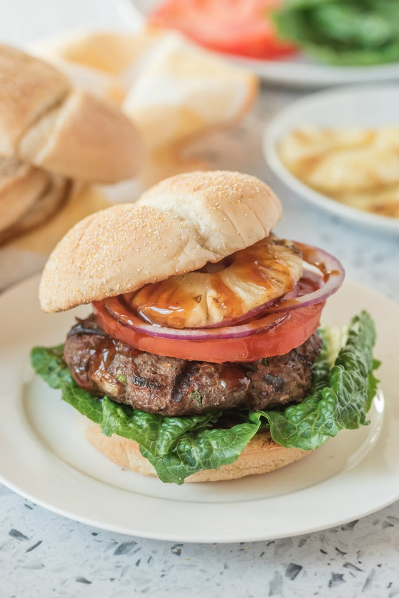 teriyaki burger with bun on top sitting on a white plate