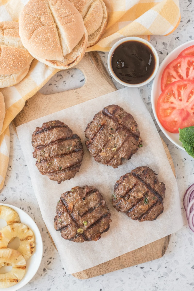 grilled teriyaki burgers with fixings surrounding on a cutting board