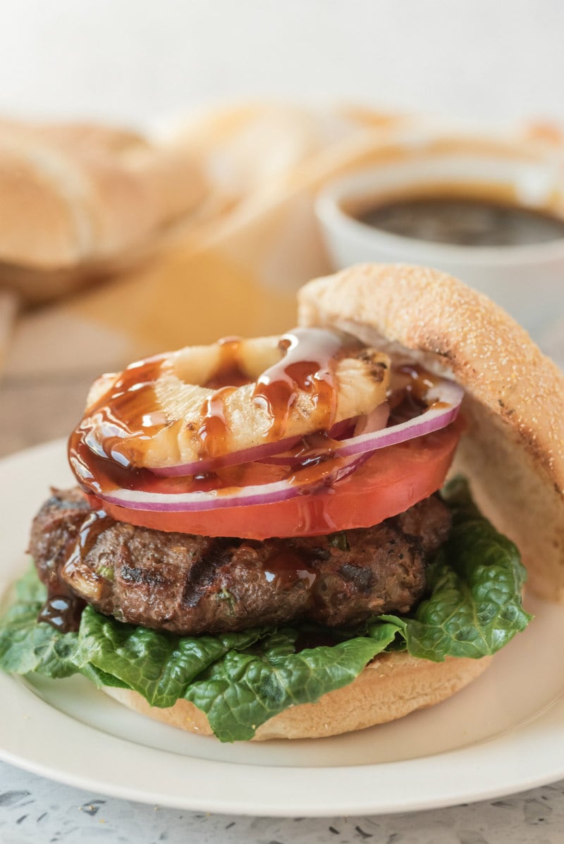 Teriyaki Burgers recipe from RecipeGirl.com #teriyaki #burger #burgers #recipe #RecipeGirl teriyaki burger with pineapple sitting on a white plate with the top of the bun slid off the top of the burger