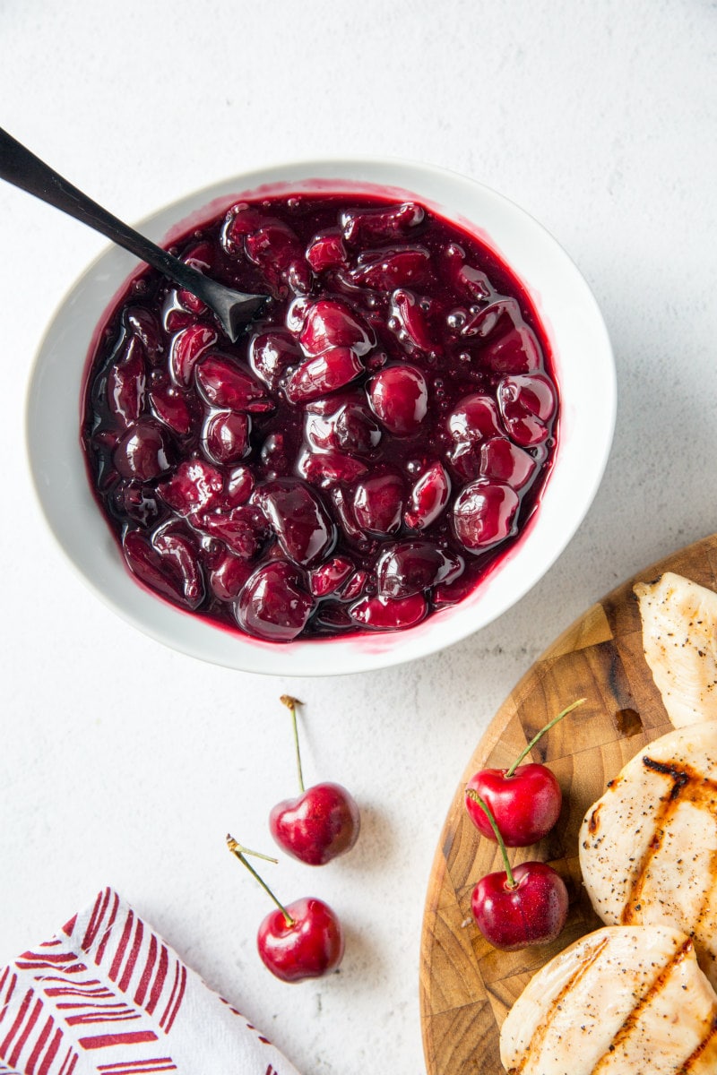 white bowl with fresh cherry sauce and a wooden board with grilled chicken and fresh cherries