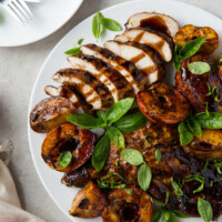 grilled chicken and peaches on a white plate with a plate of forks on the side and garnished with basil