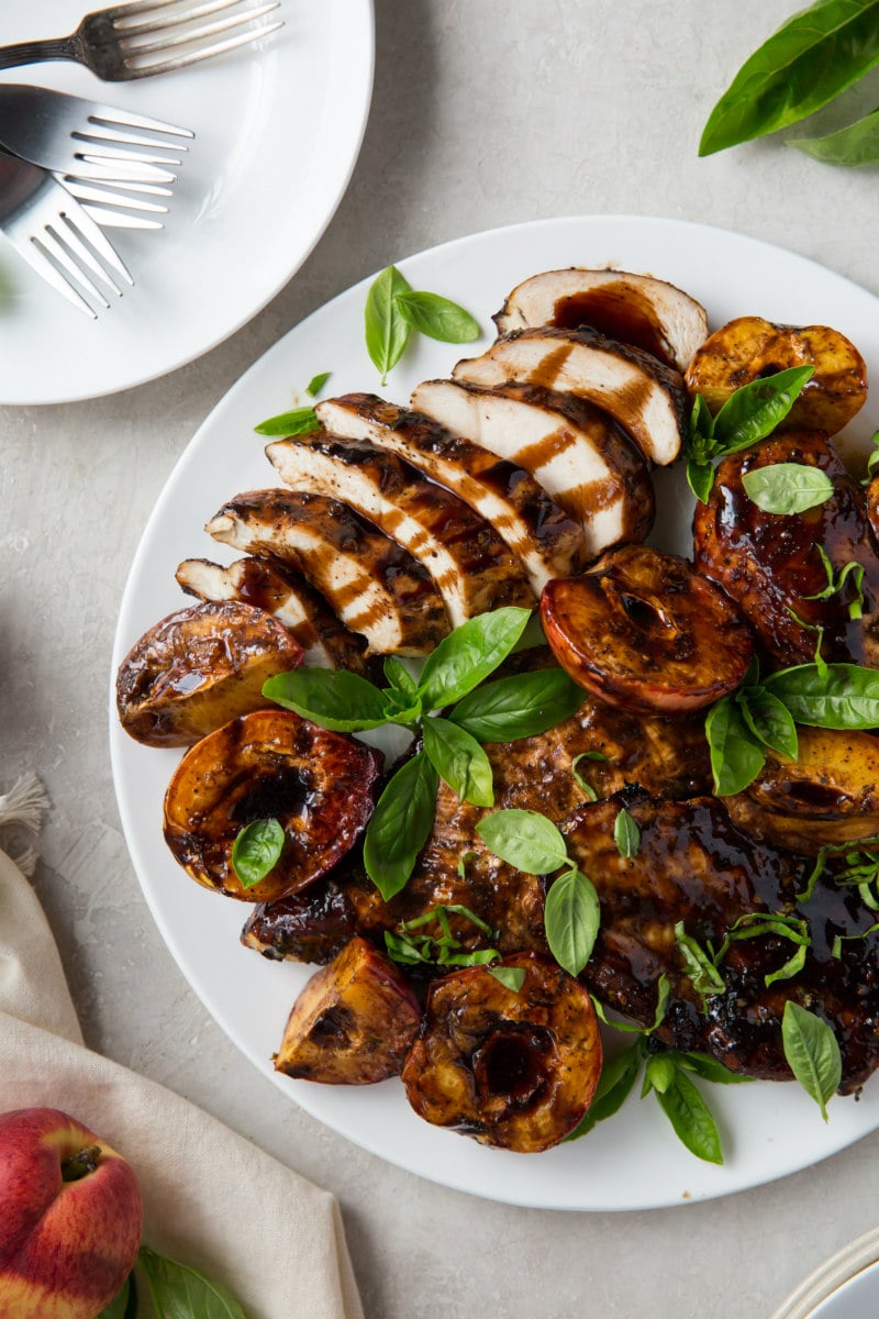 grilled chicken and peaches on a white plate with a plate of forks on the side and garnished with basil