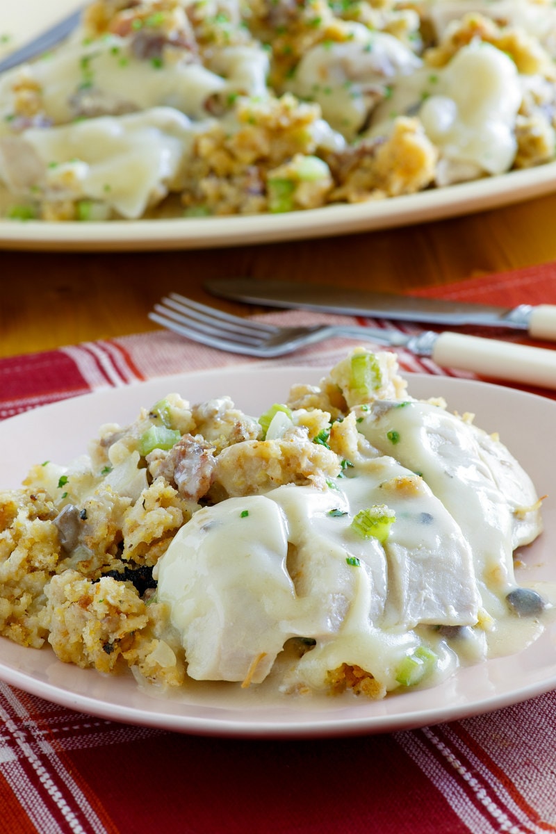 serving of Swiss Chicken Casserole on a white plate with a red plaid napkin and fork and knife - another plate of casserole in the background