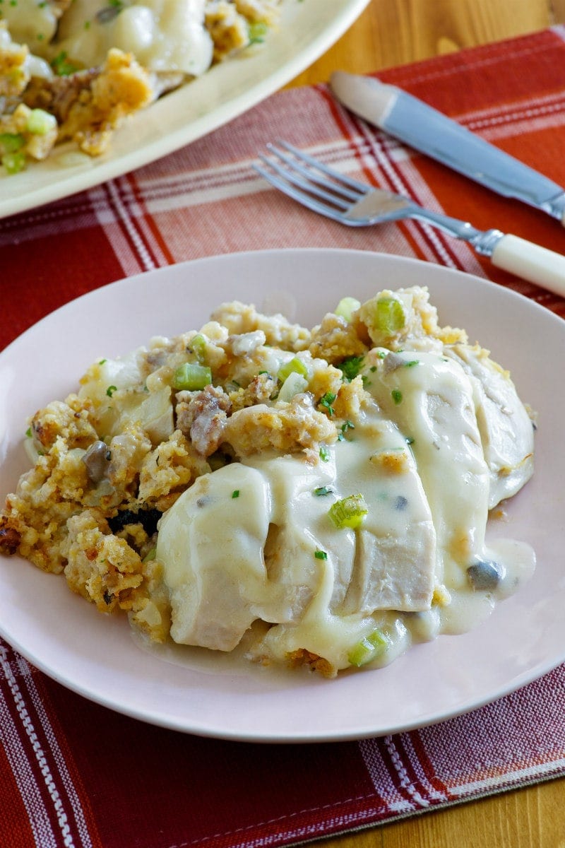 Serving of Swiss Chicken Casserole on a white plate set on a red and white plaid placemat with a fork and knife