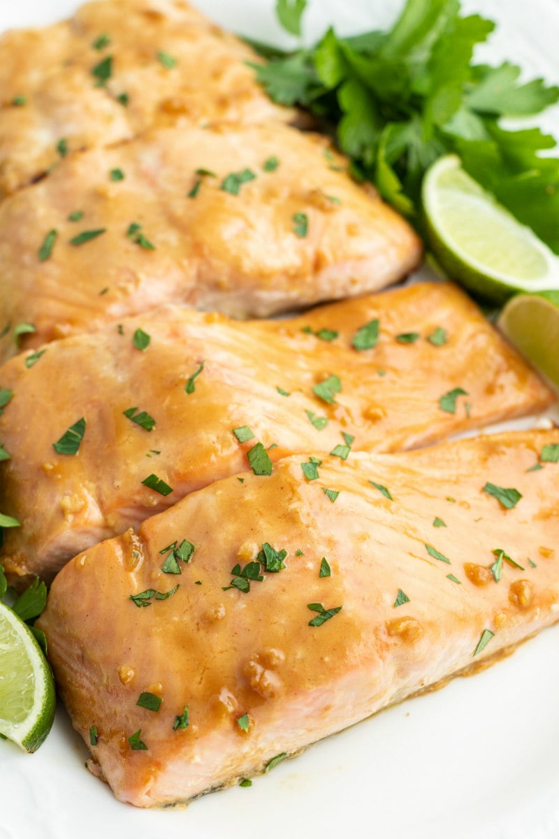 barbecued salmon cut into fillets and displayed on a white plate with parsley and lime wedges