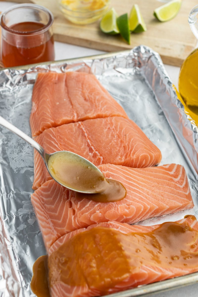 spooning marinade onto salmon filets on a foil lined baking sheet