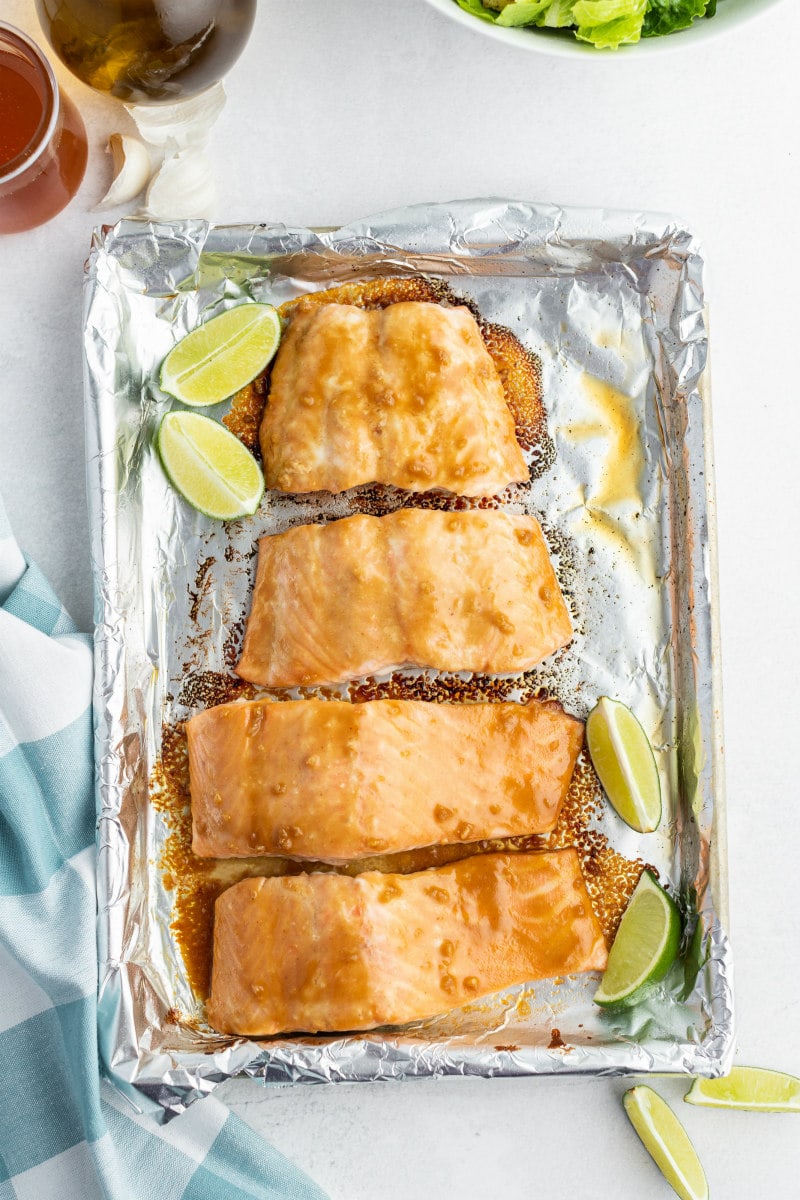 overhead shot of barbecued salmon cooked on a foil lined sheet pan with lime wedges