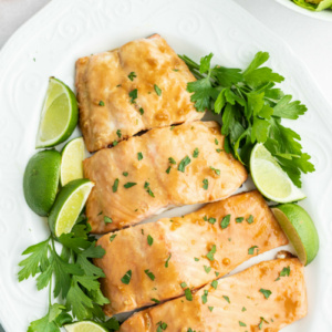 barbecued salmon cut into fillets and displayed on a white plate with parsley and lime wedges