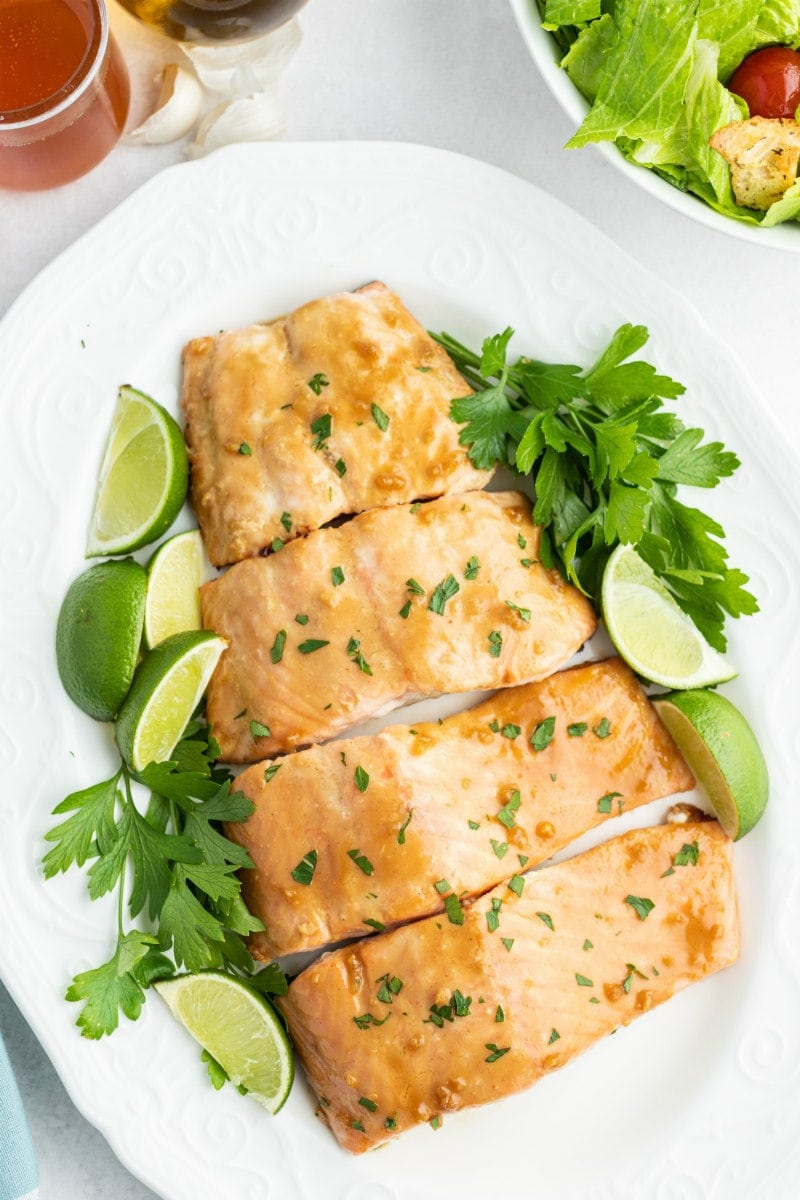 barbecued salmon cut into fillets and displayed on a white plate with parsley and lime wedges