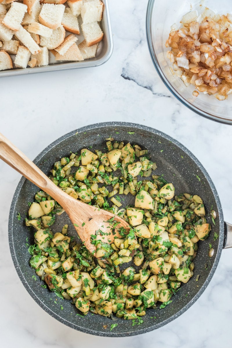 cooking chopped apples and herbs in skillet with wooden spoon