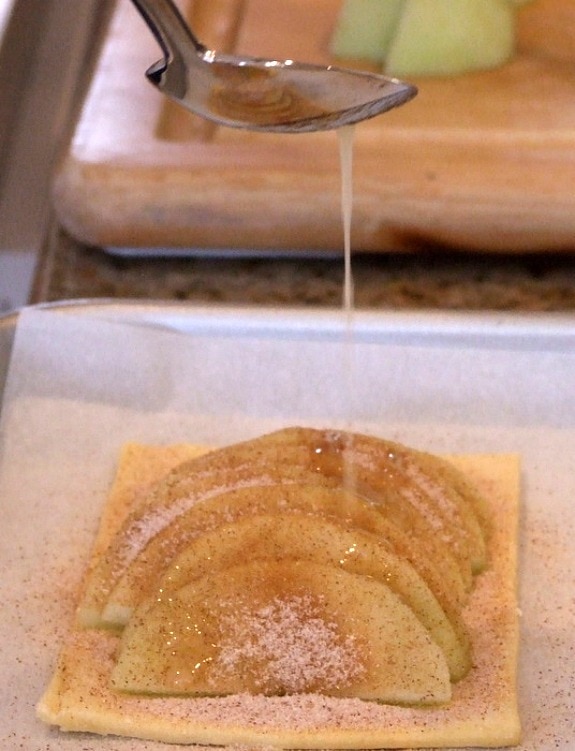 Making Maple Apple Tartlets spooning butter onto sliced apples on pastry