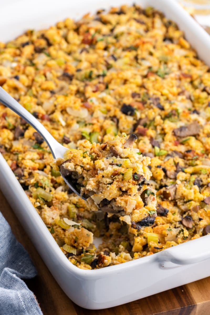 spooning stuffing out of white baking dish