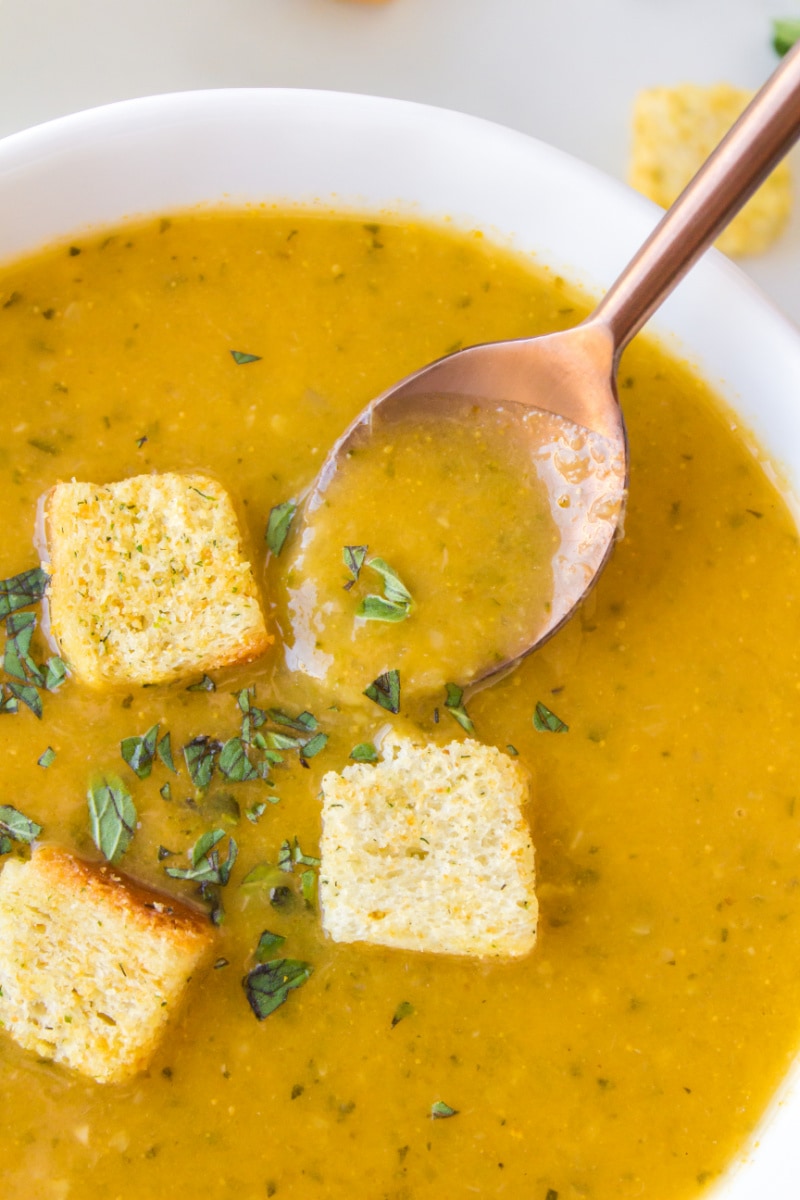 spooning out zucchini soup out of bowl with croutons
