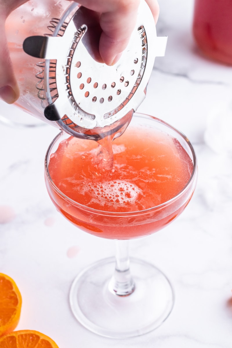 pouring cocktail into glass from shaker