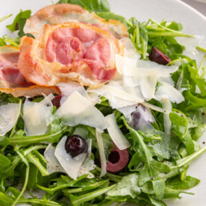plate of arugula salad with olives pancetta and parmesan