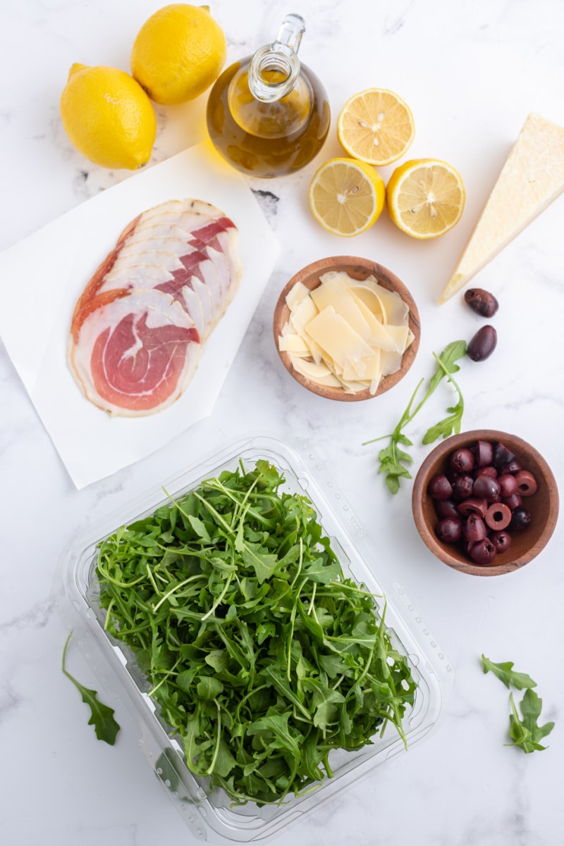 ingredients displayed for making arugula with olives pancetta and parmesan