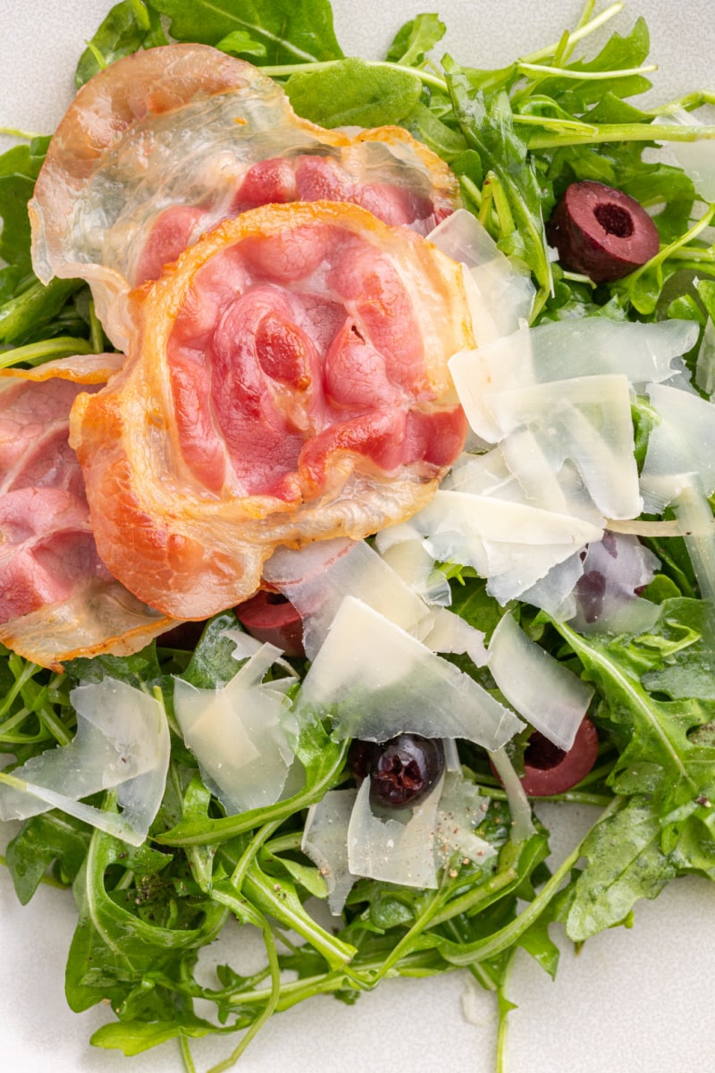 close up of arugula salad with olives, pancetta and parmesan