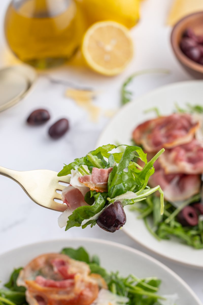fork full of arugula salad with olives pancetta and parmesan