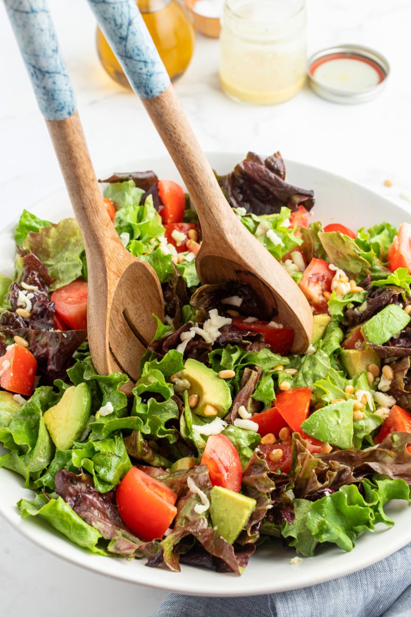 avocado pine nut salad being tossed with wooden servers