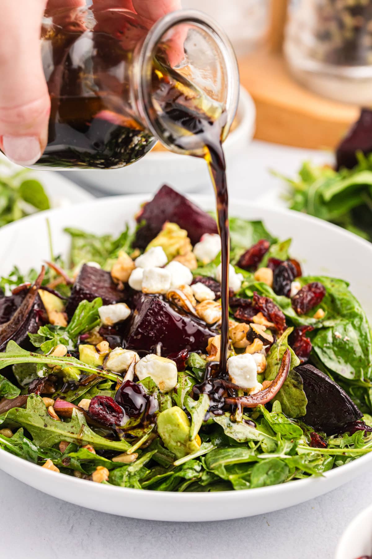 pouring dressing onto beet and goat cheese arugula salad