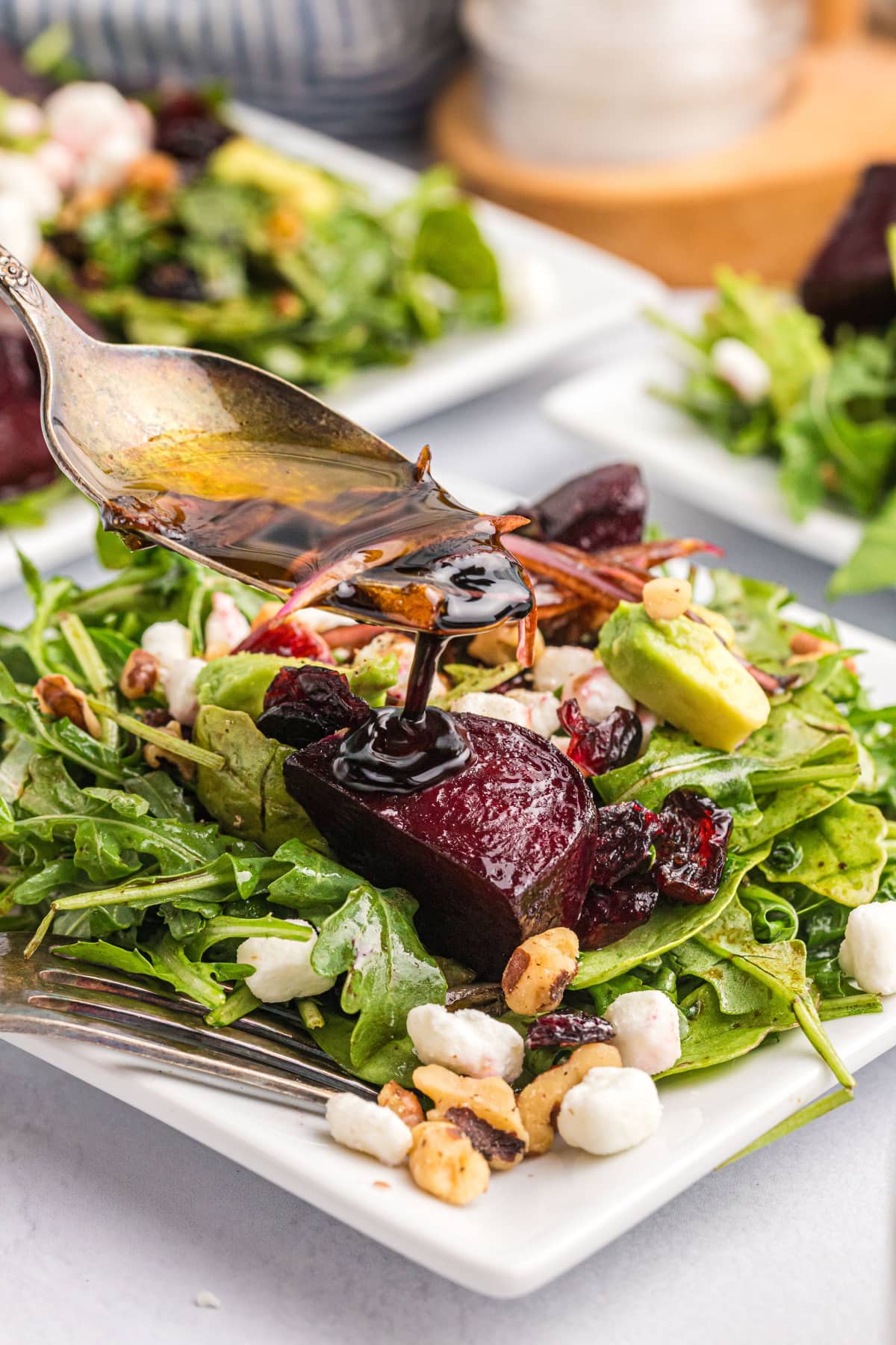 beet and goat cheese arugula salad on a plate spooning salad dressing over