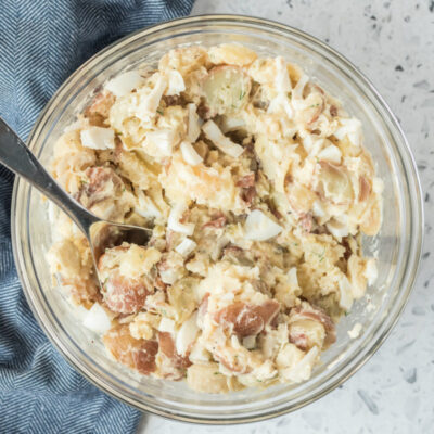 overhead shot of potato salad in a glass bowl with a serving spoon, set on a blue napkin