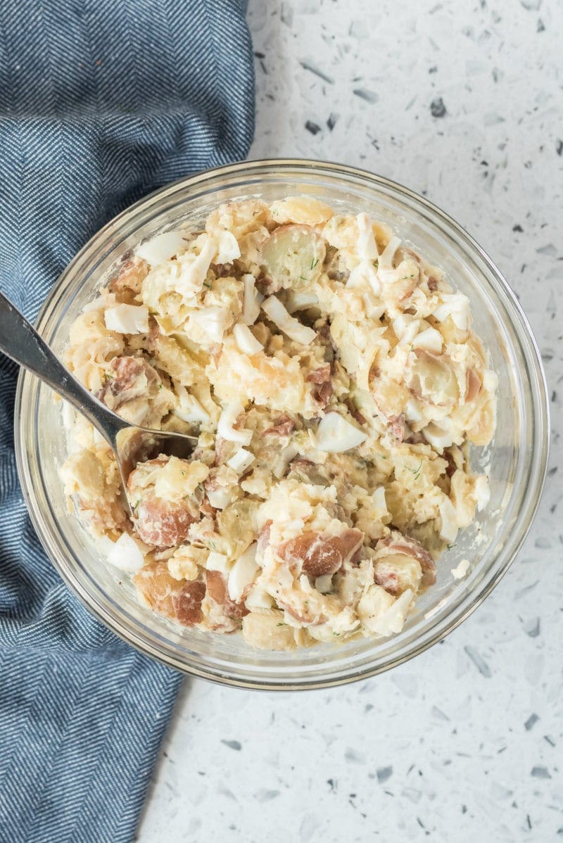 overhead shot of potato salad in a glass bowl with a serving spoon, set on a blue napkin